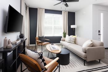 A living room with a beige sofa, a black coffee table, and a television on the wall.
